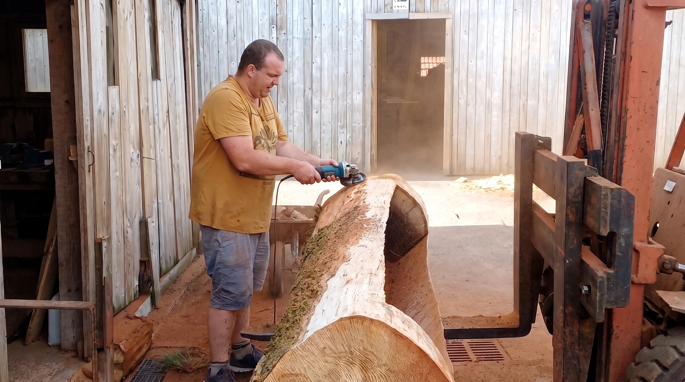 Atelier de scierie intérieur, homme en t-shirt jaune travaillant sur un tronc d'arbre massif positionné sur un chariot de scierie