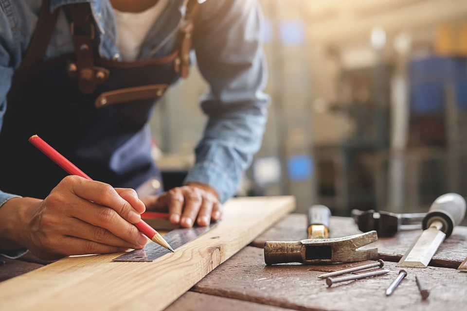 Artisan menuisier travaillant dans son atelier, manipulant une planche de bois sur établi